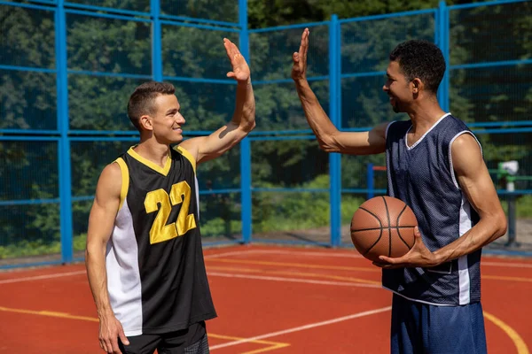 Athletic men friends on basketball court, giving high five.
