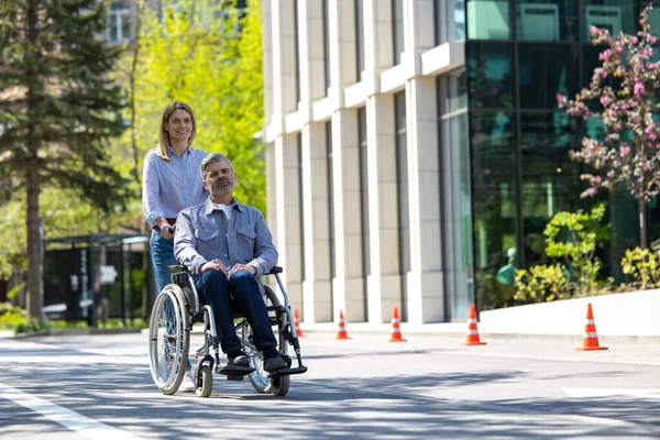 車椅子で幸せな夫と市街地を歩く愛する妻 — ストック写真