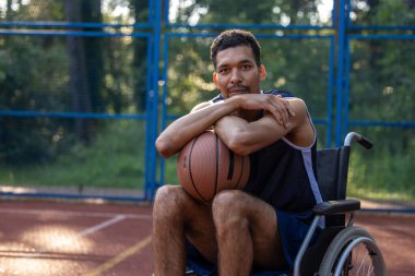 Tekerlekli sandalyedeki basketbol oyuncusunun portresi açık oyun sahasında kameraya bakıyor..