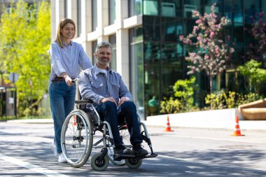 Tekerlekli sandalyede mutlu bir koca ve şehirde yürüyen sevgi dolu bir eş..