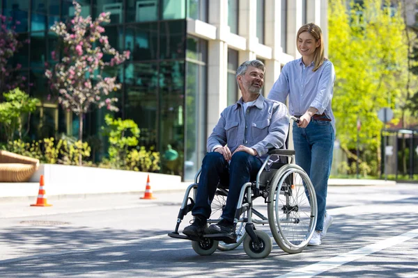 Middle aged man in wheelchair and woman walking in city street.