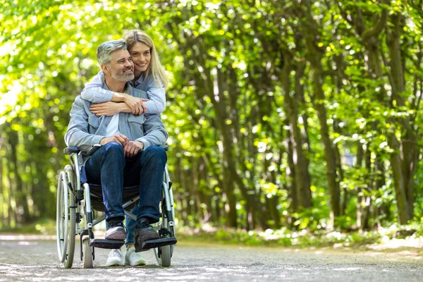 Loving Caucasian couple disabled husband in wheelchair and wife in park.