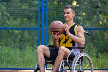 Tekerlekli sandalyedeki genç beyaz adam dışarıda basketbol oynuyor..