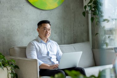 Asyalı menajer ofisteki koltukta otururken dizüstü bilgisayarında internette geziniyor..