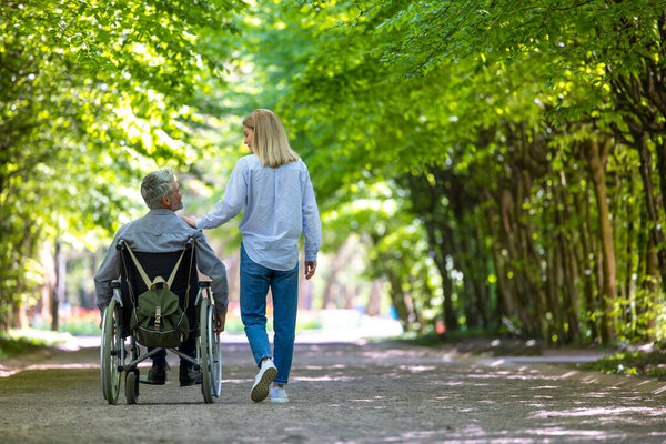 Disabled man in wheelchair walking at park with his wife.