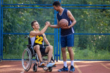 Tekerlekli sandalyedeki beyaz adam dışarıda arkadaşlarıyla basketbol oynuyor, el sıkışıyor..