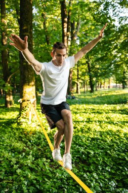 Denge. Beyaz tişörtlü ve şortlu genç adam halatı dengede tutuyor.