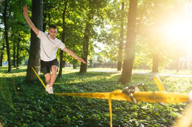Denge. Beyaz tişörtlü ve şortlu genç adam halatı dengede tutuyor.