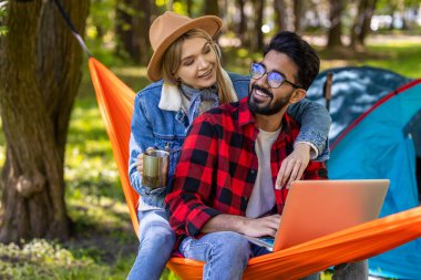 Dijital göçebe. Ormanda dizüstü bilgisayarda çalışan genç serbest çalışan, yanında kız arkadaşı olan.