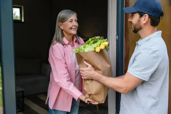 Courier man in cap delivering vegetables to woman at home.