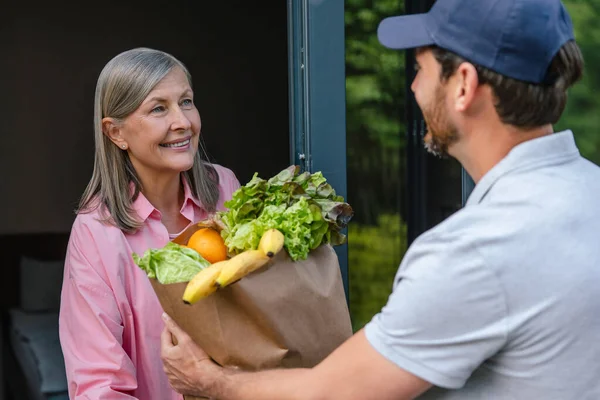 Grocery store delivery man delivering food to middle aged woman home.