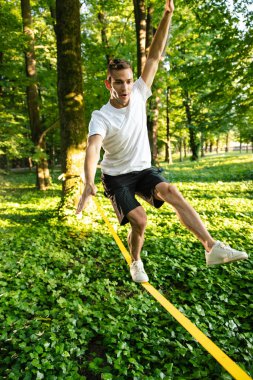 Denge. Beyaz tişörtlü ve şortlu genç adam halatı dengede tutuyor.