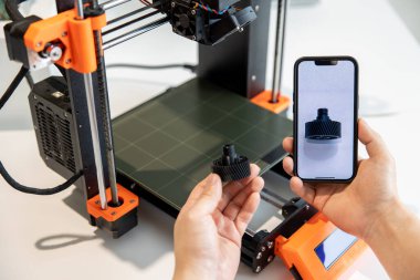 Tanımlanamayan adam ekranda detay içeren akıllı telefonu tutuyor, yaratıcı laboratuarda 3D yazıcı üzerinde çalışıyor..