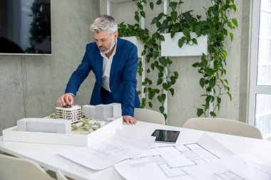 Ofiste planlar ve ev modeliyle çalışan olgun mimarlar veya mühendisler.