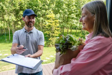 Gülümseyen kurye servis çalışanı kadın müşteriye taze yiyecek getiriyor..