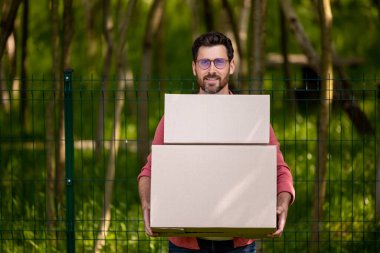 Karton kutular. Siyah saçlı, gözlüklü, kutular taşıyan genç bir adam.