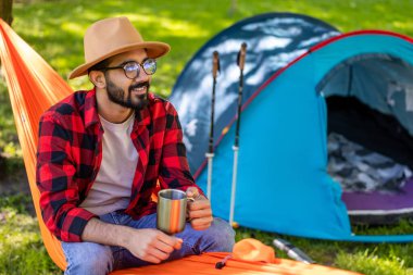 Rahatlamış hissediyorum. Hasır şapkalı sakallı genç adam hamakta rahatlamış hissediyor.