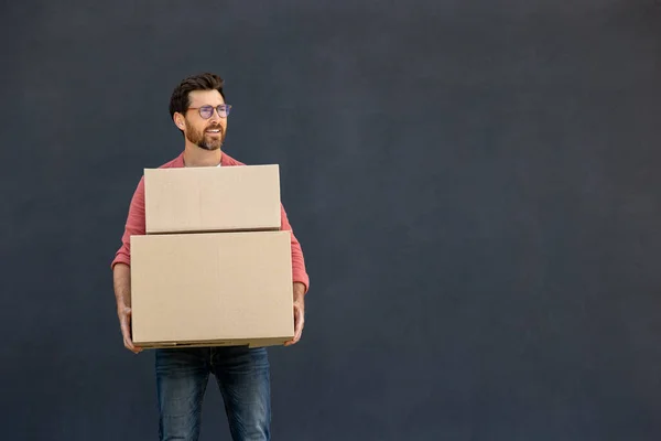 Carton boxes. Dark-haired young man in eyeglasses carrying carton boxes