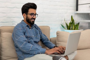 Evden çalışıyorum. Dizüstü bilgisayarda çalışan gülümseyen genç adam.