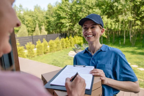 Smiling male courier delivering parcel, customer signs the delivery documents.