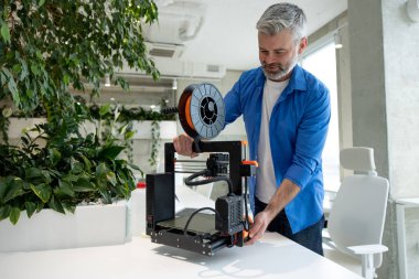 Profesyonel olgun gri saçlı tasarımcı 3D yazıcı üzerinde çalışıyor..
