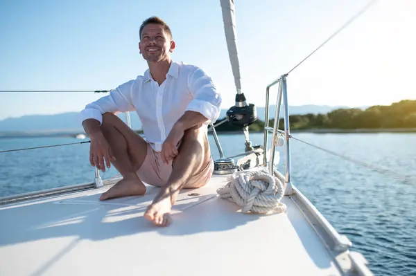 Happy man. Man in white clothes sitting on a yacht deck and looking relaxed and happy