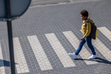 Yaya geçidinde. Kıvırcık saçlı okul çocuğu yaya geçidinden karşıya geçiyor.