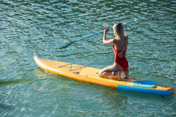 Beautiful blonde woman paddling on sup board in blue ocean.
