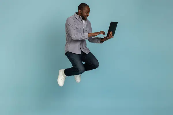 Gri Tişörtlü Neşeli Siyahi Adam Mavi Arka Planda Dizüstü Bilgisayarla — Stok fotoğraf