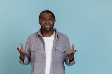 Gri gömlekli agresif siyah adam mavi arka planda tek başına duruyor.