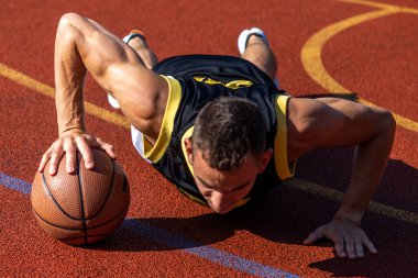 Basketbol sahasında basketbol topuyla şınav çeken yakışıklı bir genç..