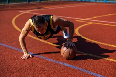 Basketbol sahasında basketbol topuyla şınav çeken atletik bir genç..