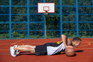 Yan bakış atletik genç adam basketbol sahasında basketbol topuyla şınav çekiyor..