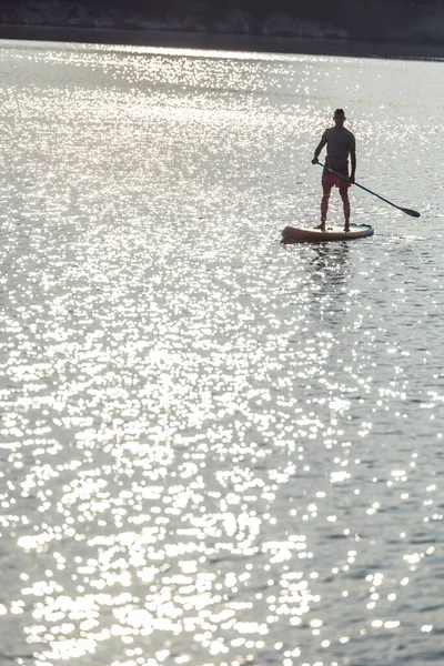 日没時に湖の真ん中にあるスーパーボード上の男のシルエット — ストック写真