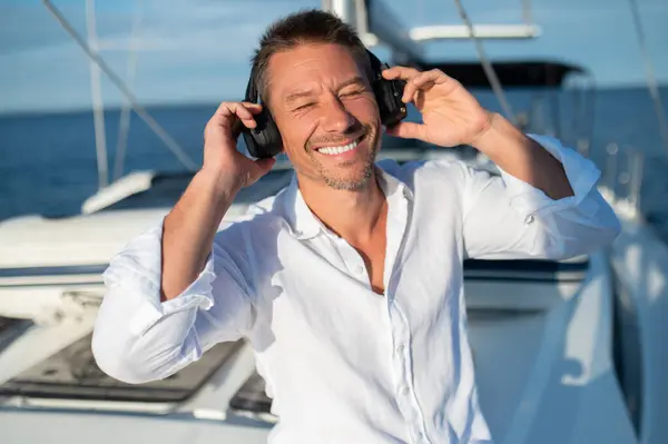 Happy and relaxed. Smiling man in headphones sailing n a yacht and looking relaxed