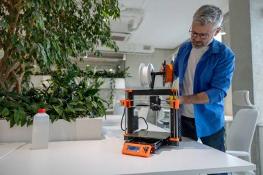 Modern 3D yazıcı ekipmanı ve ofiste çalışan olgun bir adam..