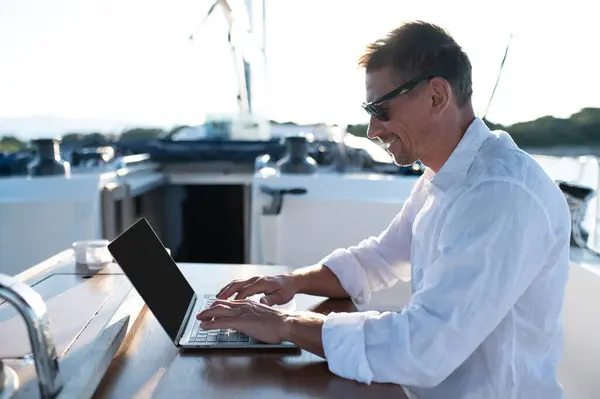 Digital nomad. Confident man in sunglasses working on a laptop while sailing on a yacht