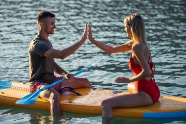 Genç ve güzel aşıklar açık okyanusta sörf tahtasında oturuyorlar..