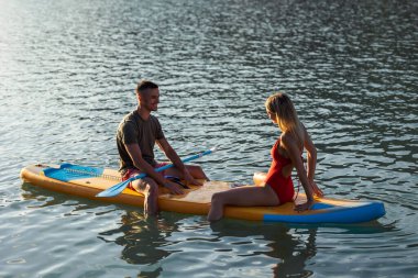 Genç ve güzel aşıklar açık okyanusta sörf tahtasında oturuyorlar..