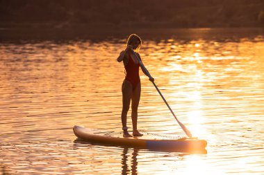 Sıska kadın silueti güneş batarken güvertede duruyor..