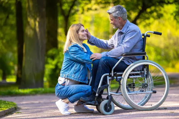 Happy couple. Man on a wheelchair having a walk in the park with his wife