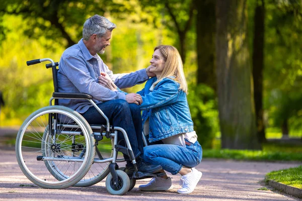 Mutlu bir çift. Tekerlekli sandalyedeki adam karısıyla parkta yürüyor.