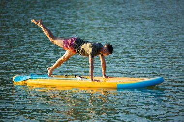Nehirdeki SUP panosunda yoga yapan bir adam..
