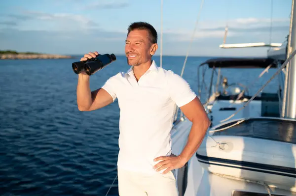On the yacht. Smiling man in white with binocular standing on the yacht
