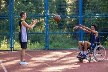 Tekerlekli sandalyedeki sporcu ve yoldaş açık hava basketbol maçının keyfini çıkarıyorlar..