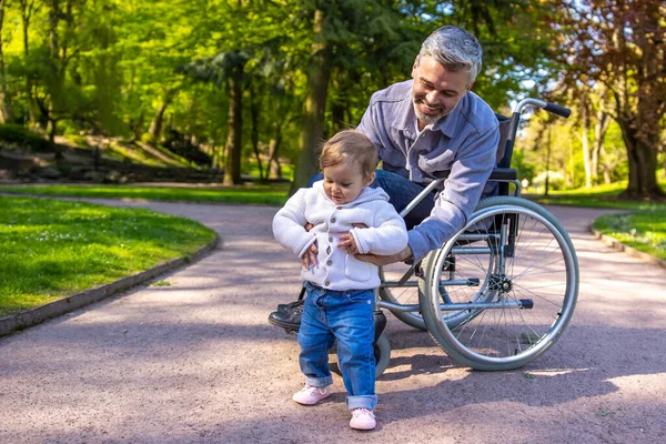 - Aile. Baba tekerlekli sandalyede oğluyla parkta oynuyor.