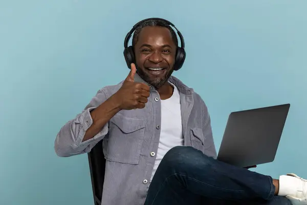 Kulaklıklı Gülümseyen Siyah Bir Adam Dizüstü Bilgisayarla Mavi Arka Planda — Stok fotoğraf