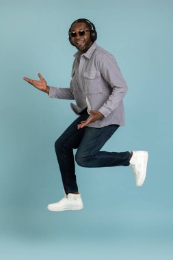 Kaygısız adam neşeli müzikler dinliyor modern stereo kulaklıklar havaya sıçrıyor mutlu bir yüz ile mavi arka planda izole edilmiş