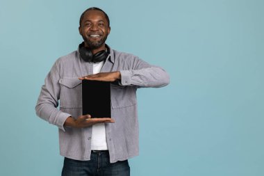 Gülümseyen siyah adam mavi arkaplan üzerinde izole edilmiş tablet boş ekran reklam alanı gösteriyor.