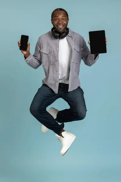 Χαρούμενος Νεαρός Άνδρας Δείχνει Tablet Και Smartphone Κενή Οθόνη Πηδώντας — Φωτογραφία Αρχείου